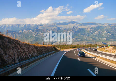 Diverse vetture su una autostrada in Croazia contro un rocky mountain range in una calda giornata estiva. Blu cielo con soffici nuvole bianche sul retro Foto Stock