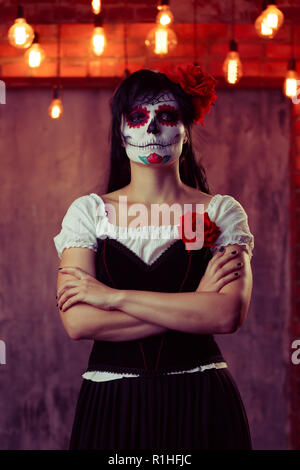 Immagine di donna zombie con il bianco per il make-up sul suo viso, cucito sulla sua bocca e occhi neri con bracci incrociati cupo sullo sfondo di un muro di mattoni con ardente lig Foto Stock