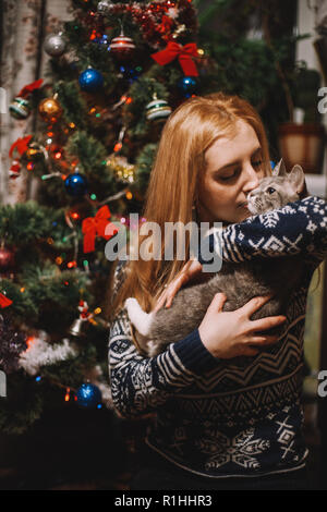 Ritratto di giovane donna seduta accanto a albero di Natale a casa giocando con cat Foto Stock