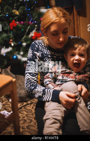 Medicazione di madre il suo bambino seduto sul pavimento a casa durante il periodo di Natale Foto Stock