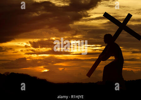 Silhouette di Gesù Cristo che porta croce su sfondo al tramonto Foto Stock