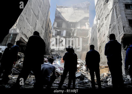 I palestinesi sono visto in piedi accanto ai resti di un edificio che è stata completamente distrutta da un attacco aereo israeliano nella striscia di Gaza City. Foto Stock