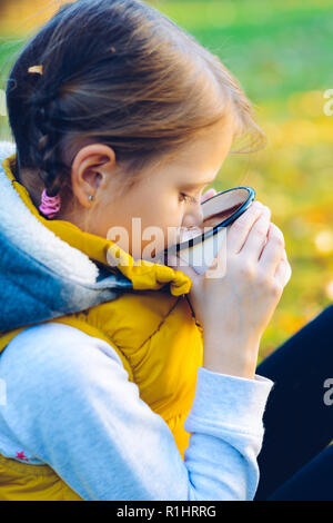 Ragazza bambino bere cioccolata in tazza vestito in un caldo giubbotto di colore giallo in autunno scenario Foto Stock