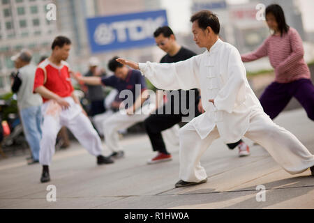 Uomo maturo indossando abiti tradizionali e mettere in pratica le arti marziali in un cortile con altri in città. Foto Stock