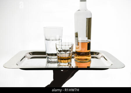 La mano del cameriere porta su un piatto d'argento, un bicchiere d'acqua, un bicchiere di alcol e una bottiglia. Isolato, copia-spazio. Foto Stock