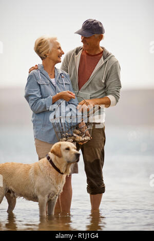 Sorridente coppia senior wading su una spiaggia con la bassa marea. Foto Stock