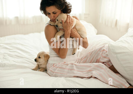Metà donna adulta abbracciando il Labrador cucciolo seduti sul letto. Foto Stock