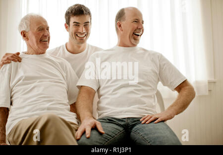 Tre uomini di un multi famiglia generazionale ridere insieme all'interno di una stanza. Foto Stock