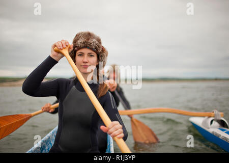 Ritratto di una giovane donna che indossa un cappello di pelliccia e muta mentre paddling in canoa con amici. Foto Stock