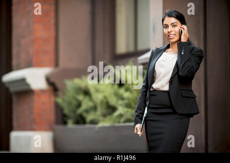 Fiducioso giovane imprenditrice chat sul suo telefono cellulare mentre cammina lungo la strada. Foto Stock