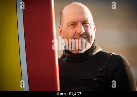 Ritratto di un sorridente metà uomo adulto in piedi con la sua tavola da surf sotto il sole. Foto Stock