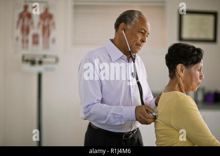 Medico maschio ascoltare il battito del cuore di una femmina matura paziente dentro il suo ufficio. Foto Stock