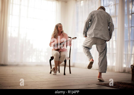 Senior man dancing mentre sua moglie riproduce una chitarra. Foto Stock