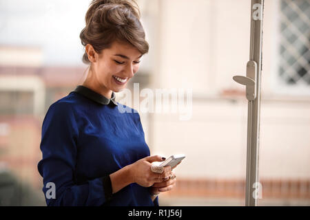 Sorridente giovane imprenditrice utilizzando un telefono intelligente. Foto Stock