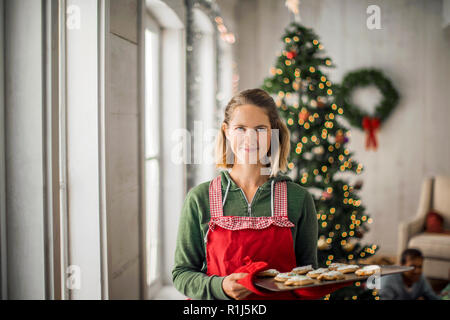 Ritratto di una donna sorridente tenendo un vassoio di pane appena sfornato, biscotti di Natale. Foto Stock