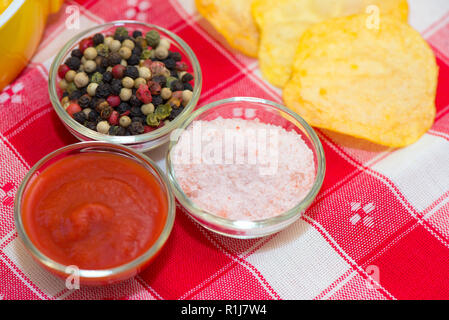 Ketchup, sale pepe in ciotole e i chip sulla tovaglia Foto Stock