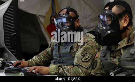 Stati Uniti Army Spc. Rene Cortez, analista di intelligence, e CPT. Gary Suen, vigili del funzionario di intelligence, entrambi assegnati alla 224th supporto brigata, California Army National Guard, indossare il M50 Servizio comune scopo generale maschera mentre svolgono le loro mansioni durante Warfighter 19-1 a Camp Atterbury, Indiana, Ottobre 8, 2018. Cortez e Suen ha rispolverato le loro maschere di protezione come parte di un warfighter esercitazione. Foto Stock