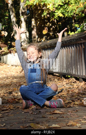 Giovane ragazza che gioca con le foglie in autunno Foto Stock