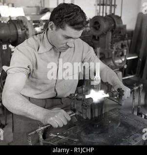 Degli anni Cinquanta, storico, un esperto lavoratore di sesso maschile in corrispondenza di un banco da lavoro servendosi di bruciatori a gas per produrre engineering parti in vetro, Inghilterra, Regno Unito. Foto Stock