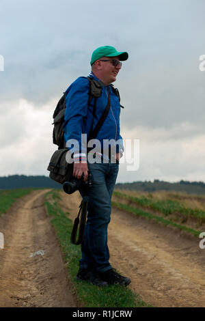 Sport giovane in una giacca a vento cappuccio e jeans con una macchina fotografica in mano sorge su di un sentiero in alta montagna Foto Stock