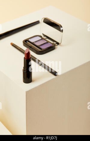 Close-up shot di rossetto con viola eyeshadows caso e spazzole sul beige Foto Stock