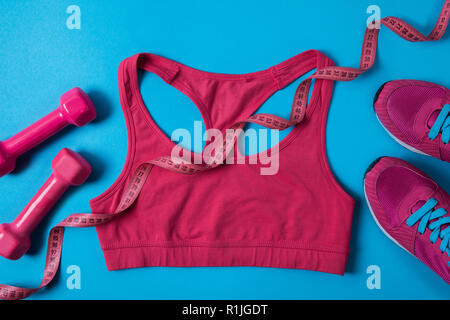 Vista superiore della rosa manubri, nastro di misurazione, sport bra e sneakers isolato su blu Foto Stock