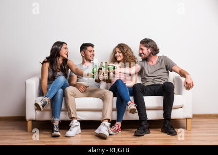 Ritratto di giovane gruppo di amici seduti su un divano in un studio, il tintinnio delle bottiglie. Foto Stock