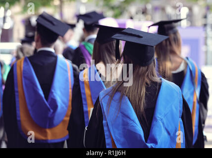 Laureati presso università cerimonia indossando mortarboard e vestaglia Foto Stock