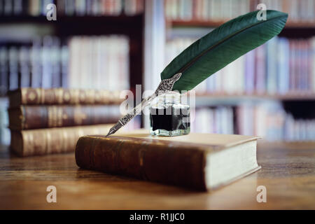 Quill penna e inchiostro ben appoggiato su un vecchio libro in una libreria concetto per la letteratura, la scrittura, autore e storia Foto Stock