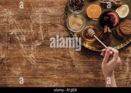 Immagine ritagliata della donna azienda miele stick al tavolo di legno Foto Stock