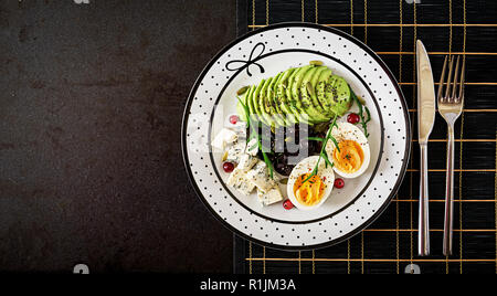 Uno spuntino o una sana colazione - piastra di formaggio blu, avocado, uova sode, olive su uno sfondo nero. Vista superiore Foto Stock