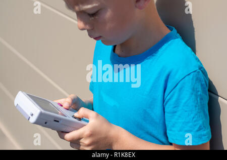 Ragazzo con il suo Nintendo Gameboy per giocare con i videogame sul computer. Impostazione degli anni novanta. all'aperto l'impostazione. Foto Stock