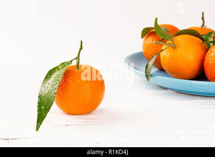 Tangerini bianco su sfondo di legno con gocce d'acqua un foglie verdi Foto Stock