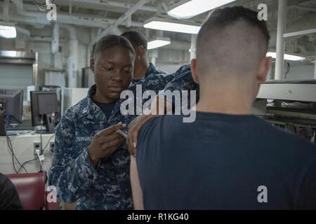 SAN DIEGO (ott. 16, 2018) Ospedale Corpsman 3rd Class misericordia Onwunta, dal Bronx, N.Y., amministra un virus influenzale vaccino per Aviation Electronics Technician Airman Nicholas Myers, di Greenville, Ohio, nel reparto di medicina a bordo dell'assalto anfibio nave USS Bonhomme Richard (LHD 6). Bonhomme Richard è nel suo homeport di San Diego. Foto Stock