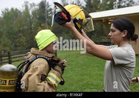 Stati Uniti Air Force Airman 1. Classe Brianna Espino, un pompiere assegnato al centottantesimo Fighter Wing, Ohio Air National Guard, aiuta a Noè latti, un boy scout di truppa 263 fuori di Toledo, Ohio, ottenere vestito in un vigile del fuoco la tuta durante il Camp Frontier cinquantesimo anniversario camporall 6 ott. 2018 in Pioneer, Ohio. Avieri dal centottantesimo Fighter Wing, Ohio Air National Guard si sforzano di dare di più per la comunità che essi ricevono. Foto Stock