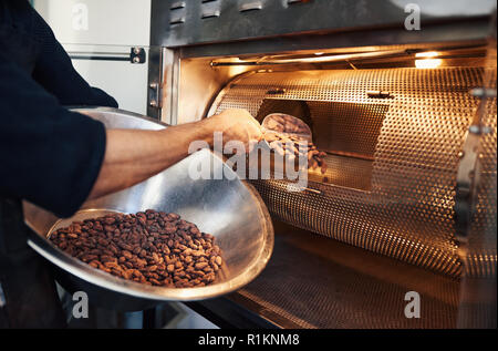 La produzione del cioccolato operaio di fabbrica mettendo le fave di cacao in un girarrosto Foto Stock