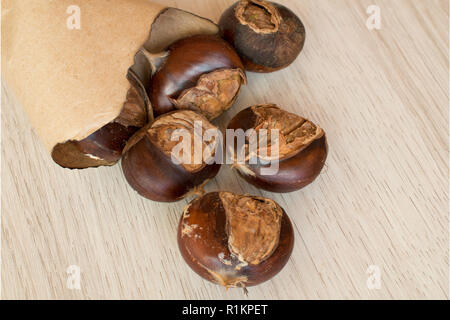 Varie castagne arrostite nel sacchetto di carta su un sfondo di legno Foto Stock