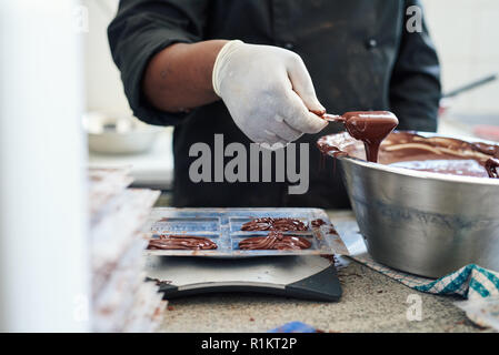 Dolciumi rendendo operaio di fabbrica di mettere il cioccolato fuso in stampi Foto Stock