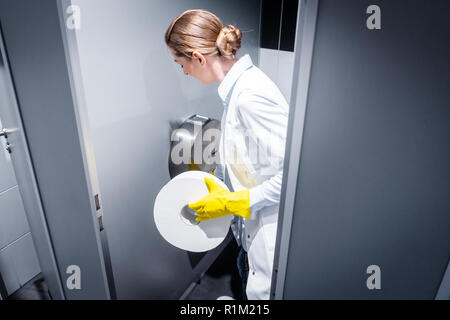 Donna bidello di sostituzione della carta in un bagno pubblico o toilette Foto Stock