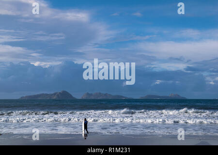 Surfer proveniente dall'acqua sulla riva della spiaggia Foto Stock