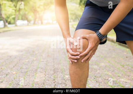 Sport uomo che soffre il ginocchio della gamba e di ferire come esercizio e allenamento nel parco Foto Stock