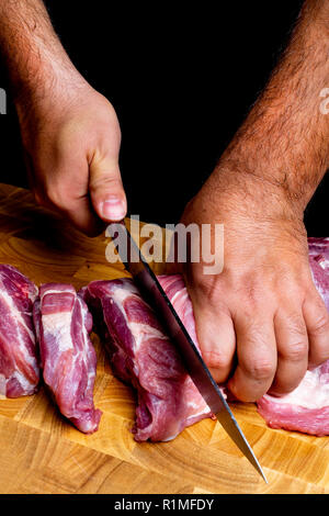 Professional mani dell'uomo il taglio di carne di maiale cruda sulla tavola di legno, fuoco selettivo, close-up Foto Stock