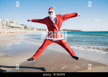 Un giovane uomo caucasico in una santa suit salta sulla spiaggia Foto Stock