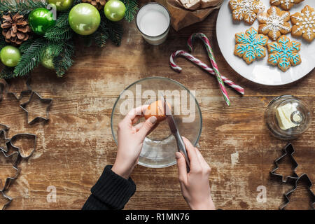 Ritagliato colpo di cracking donna uovo di pollo in un recipiente mentre si effettua la pasta per biscotti di Natale sul tavolo in legno con corona decorativa Foto Stock