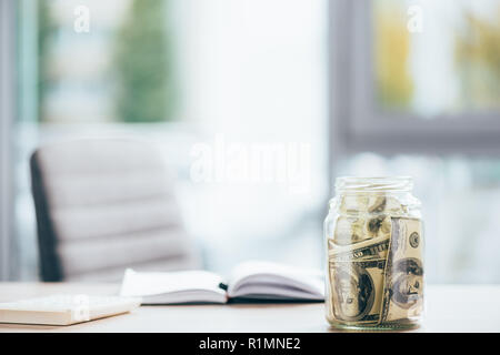 Vista ravvicinata di un barattolo di vetro con banconote di dollari sul tavolo per ufficio Foto Stock