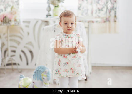 Concetto di infanzia. Baby girl in abito carino ubicazione a letto a giocare con i giocattoli da casa. Bianco childroom vintage Foto Stock