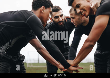 I giocatori di calcio di unire le vostre mani in huddle parlando della strategia di gioco. Basso angolo di visione dei calciatori la piegatura in avanti in un huddle tenendo le mani. Foto Stock