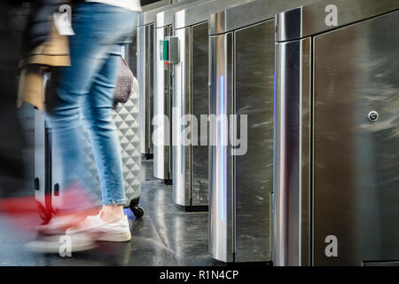 Vista laterale di una donna con una valigia scorrevole passando per acciaio inox cancelli di ticket in un trasporto pubblico dalla stazione di Parigi con motion blur Foto Stock