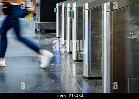 Vista laterale di una giovane donna che passa attraverso in acciaio inox cancelli di ticket in un trasporto pubblico dalla stazione di Parigi, Francia, con motion blur. Foto Stock