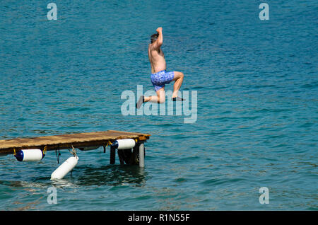 Uomo in costume da bagno con un tuffo nel mare da un molo in legno, vestita di nero scarpe di gomma Foto Stock